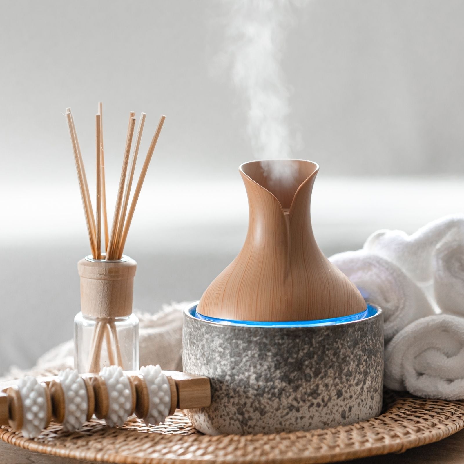 Moderner Diffusor aus Holz verströmt feinen Nebel – eingerahmt von Handtüchern, Stäbchen und ruhiger Spa-Atmosphäre. Symbolbild für die Anwendung ätherischer Öle im Alltag.