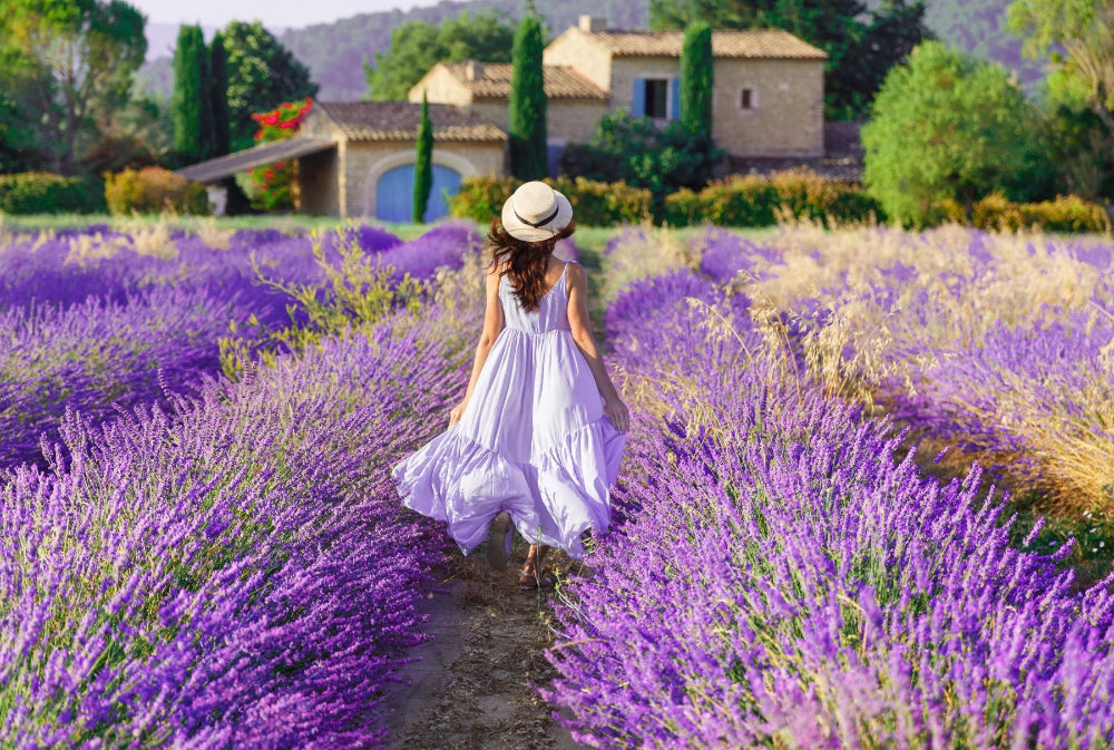 Frau in weißem Sommerkleid spaziert durch ein blühendes Lavendelfeld in der Provence – Symbol für Ruhe, Harmonie und die natürliche Kraft der Lavendelöle von ESSENCE-PUR.