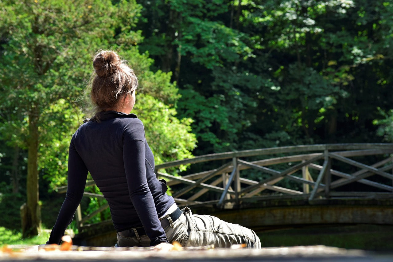 Frau sitzt entspannt vor einer Holzbrücke im Wald – Symbol für Ruhe, Naturverbundenheit und Einklang mit der Natur. (Foto: Silvia Rita, Pixabay)