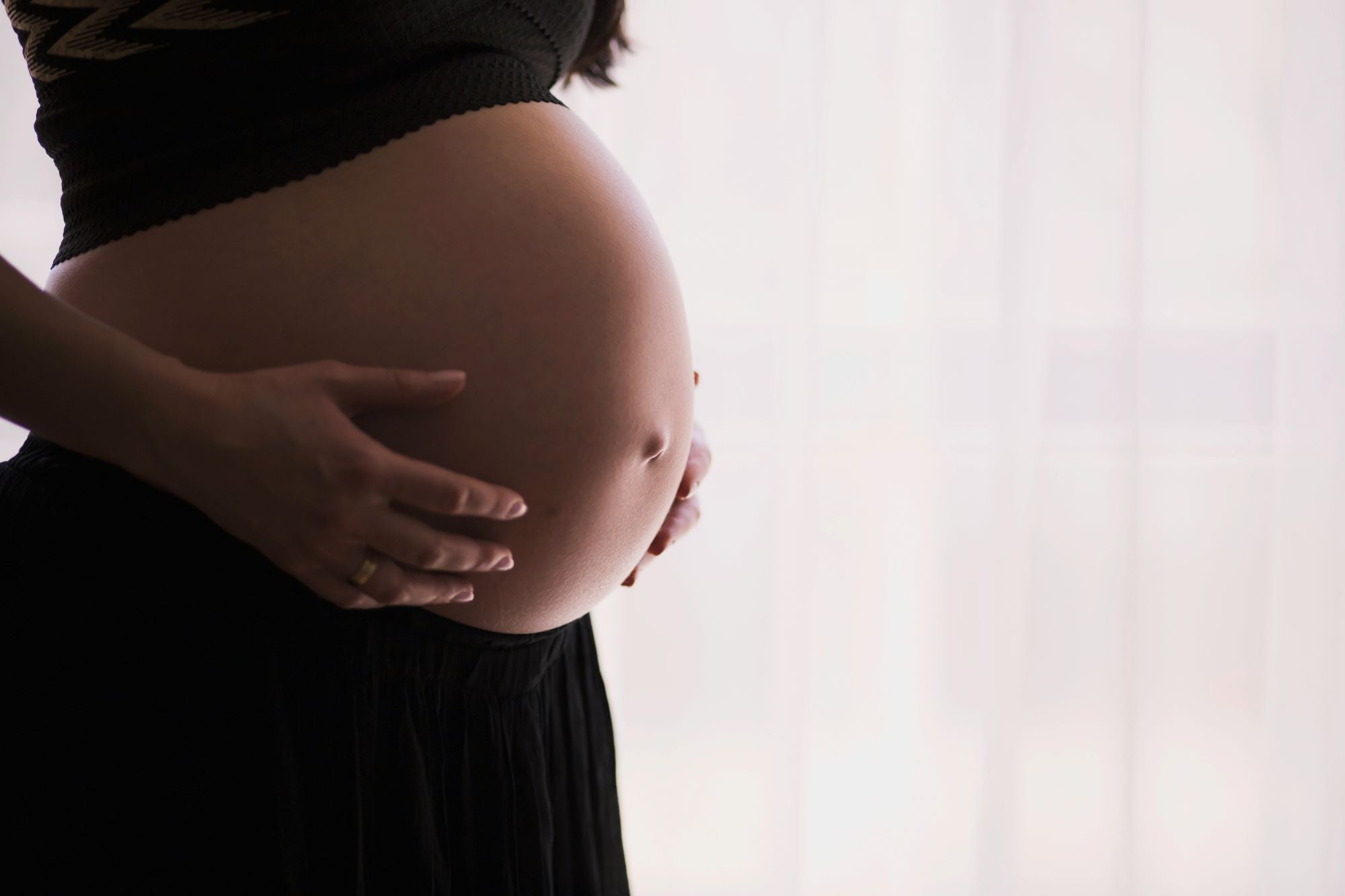 Schwangere Frau hält schützend ihre Hände auf den nackten Bauch – Symbol für Geborgenheit und natürliche Fürsorge