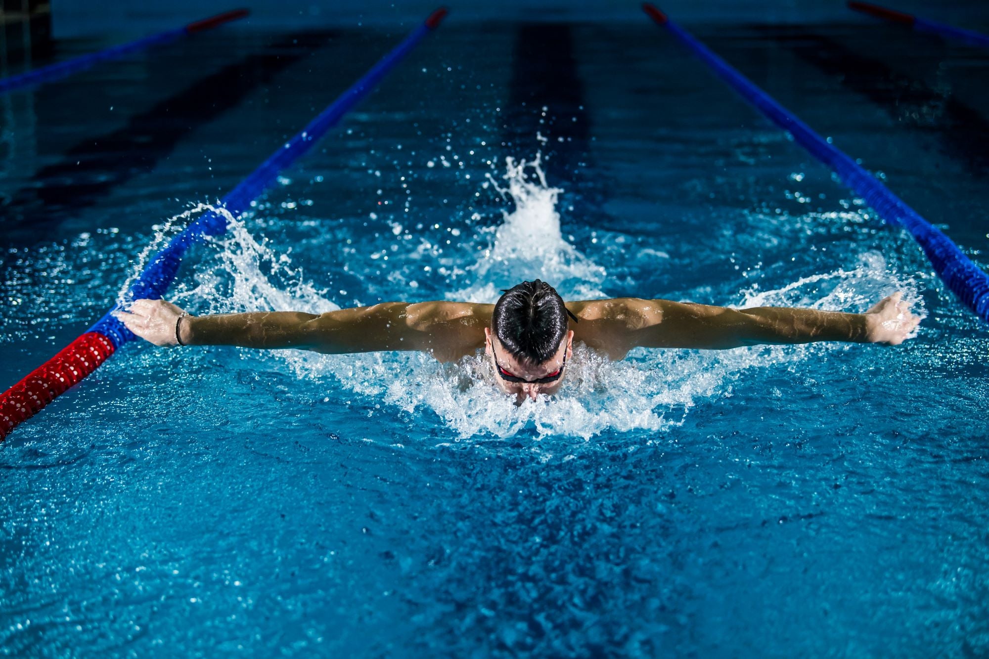 Leistungsstarker Schwimmer beim Butterfly-Stil in einem klaren blauen Becken – symbolisiert Energie, Fokus und körperliche Stärke.