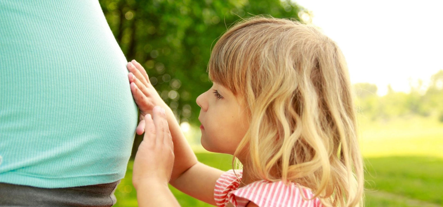 Kleines Kind legt zärtlich die Hände auf den Babybauch seiner Mutter – zarte Verbindung, Liebe und Vorfreude auf neues Leben