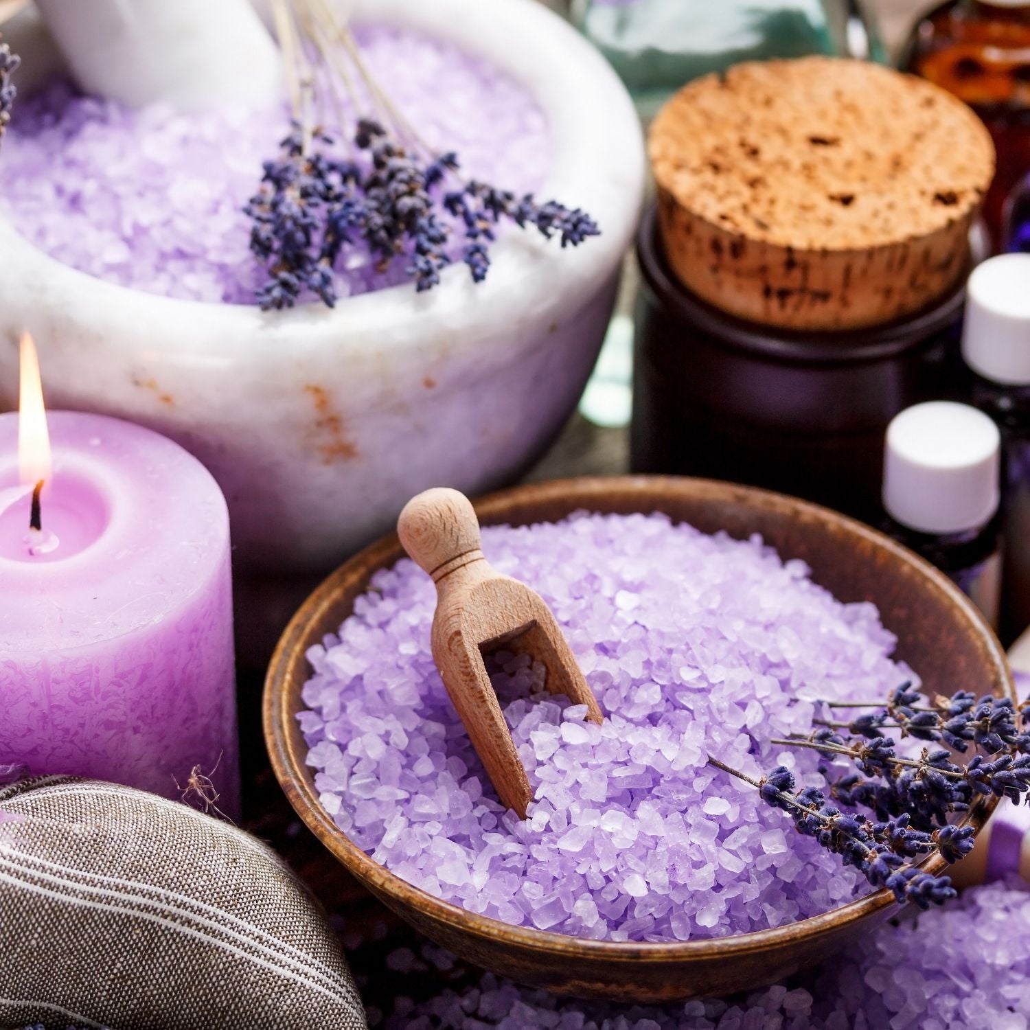Lavendel Wellness – violette Badesalze, Kerze und ätherische Lavendelblüten als Symbol für Entspannung und Aromatherapie – ESSENCE-PUR
