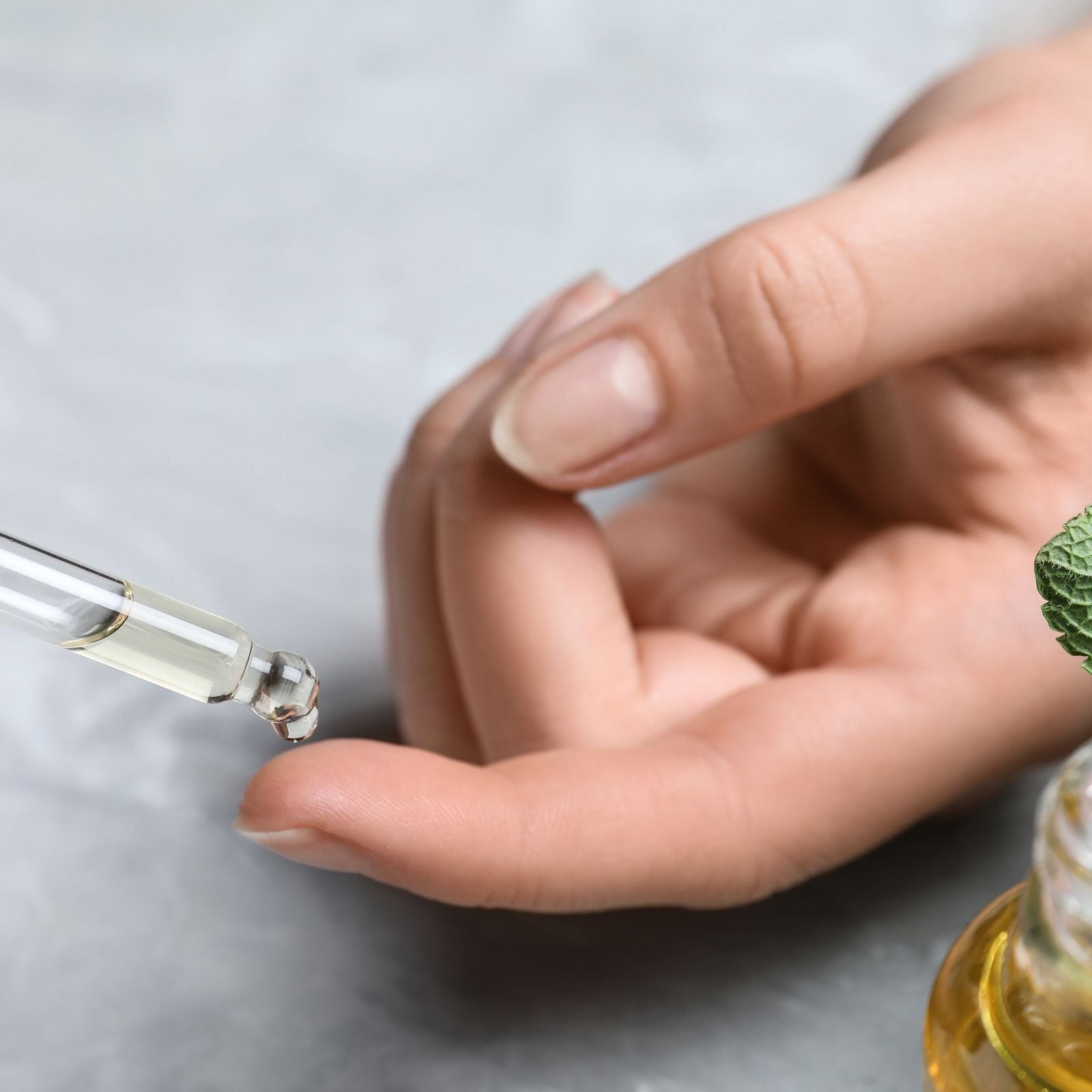 Nahaufnahme einer Hand, auf die ein Tropfen ätherisches Öl aus einer Pipette fällt – Symbol für sanfte, achtsame Anwendung und die Wirkung ätherischer Öle auf Körper und Seele.