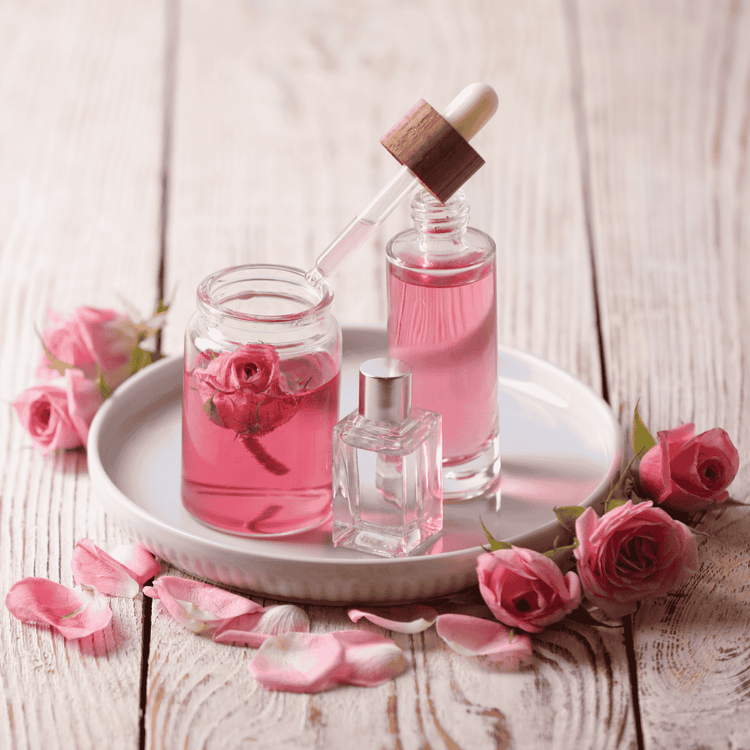 Glasflaschen mit Rosenöl und Pipette, dekoriert mit frischen Rosenblüten auf Holzuntergrund – Symbol für natürliche Aromapflege.