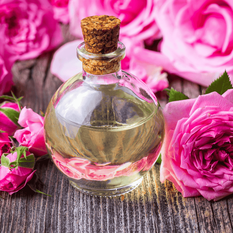 Runde Glasflasche mit Rosenöl umgeben von rosafarbenen Rosenblüten – hochwertige Essenz aus der Damaszenerrose.