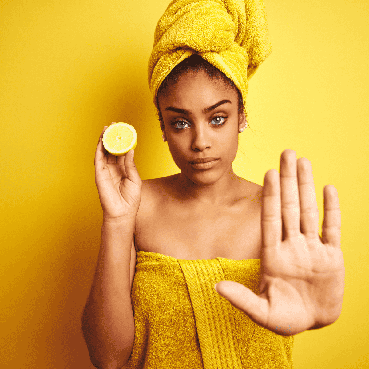 Frau im gelben Handtuch mit Zitrone und erhobener Hand – Darstellung der Sicherheitshinweise zu ätherischem Zitronenöl.