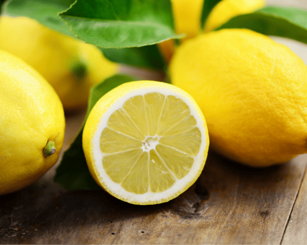 Frische gelbe Zitronen mit halbierter Frucht und grünen Blättern auf einem Holztisch – Symbol für die natürliche Frische von Zitronenöl.