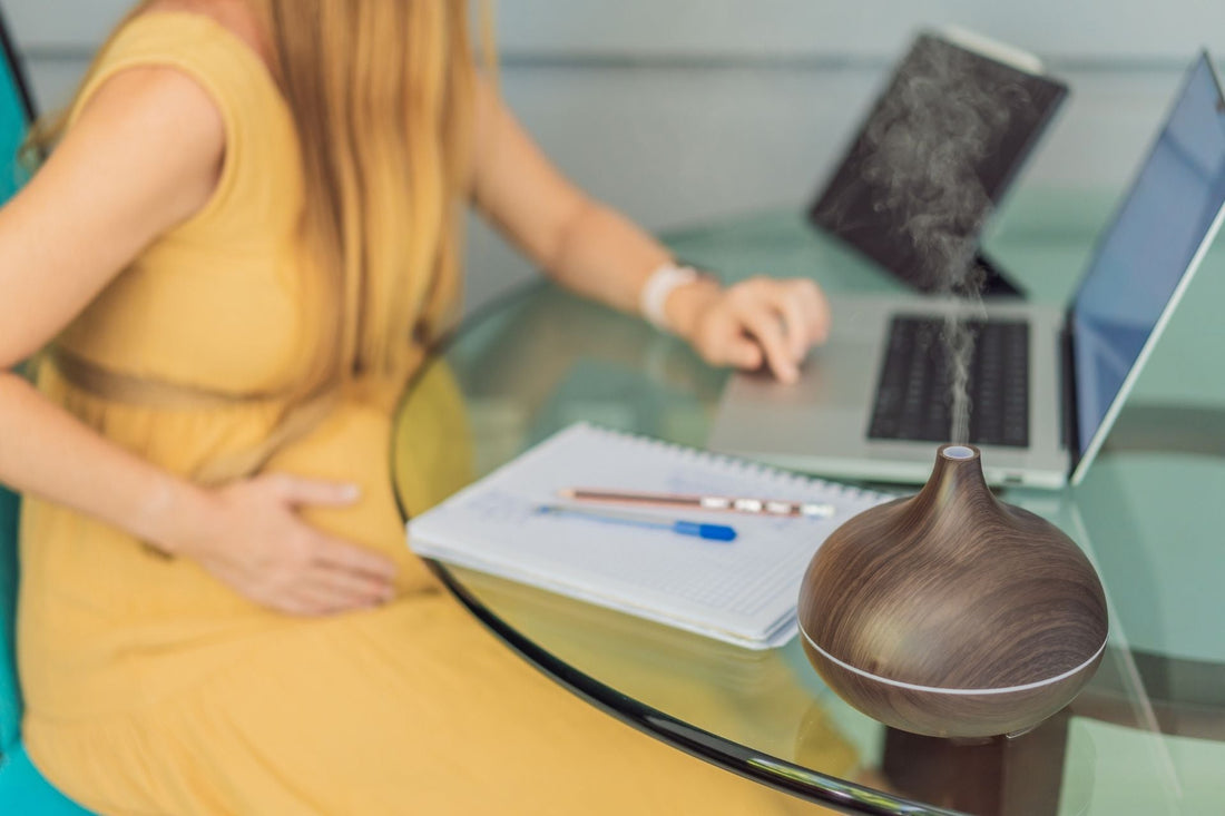Schwangere Frau am Laptop mit Notizbuch und Duftdiffuser – ätherische Öle schaffen Wohlbefinden am Arbeitsplatz