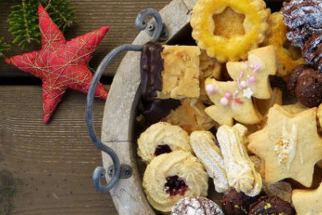 Bunter Teller mit verschiedenen Weihnachtsplätzchen in Stern-, Herz- und Blumenform auf Holzuntergrund – dekoriert mit Tannenzweigen und rotem Stern. Symbol für festliche Backfreude und Genuss zur Weihnachtszeit.