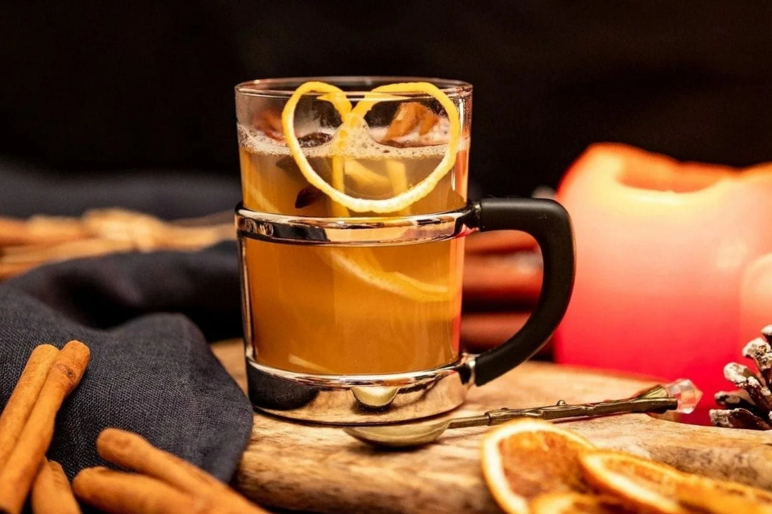 Winterliches Stillleben mit Gewürztee in Glas mit Zitronenzeste, Zimtstangen, getrockneten Orangenscheiben und roten Kerzen – vermittelt Wärme, Geborgenheit und winterliche Aromavielfalt.