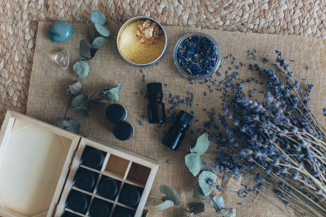 Selbstgemachte Geschenkideen mit ätherischen Ölen – auf Naturfaseruntergrund arrangiert mit kleinen Fläschchen, getrocknetem Lavendel, Blüten und Kräutern. Symbol für DIY-Kosmetik und duftende Wohlfühlgeschenke.