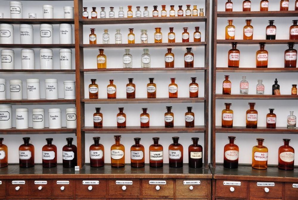 Historische Hausapotheke mit beschrifteten Glasflaschen und Apothekengefäßen in traditionellem Regal