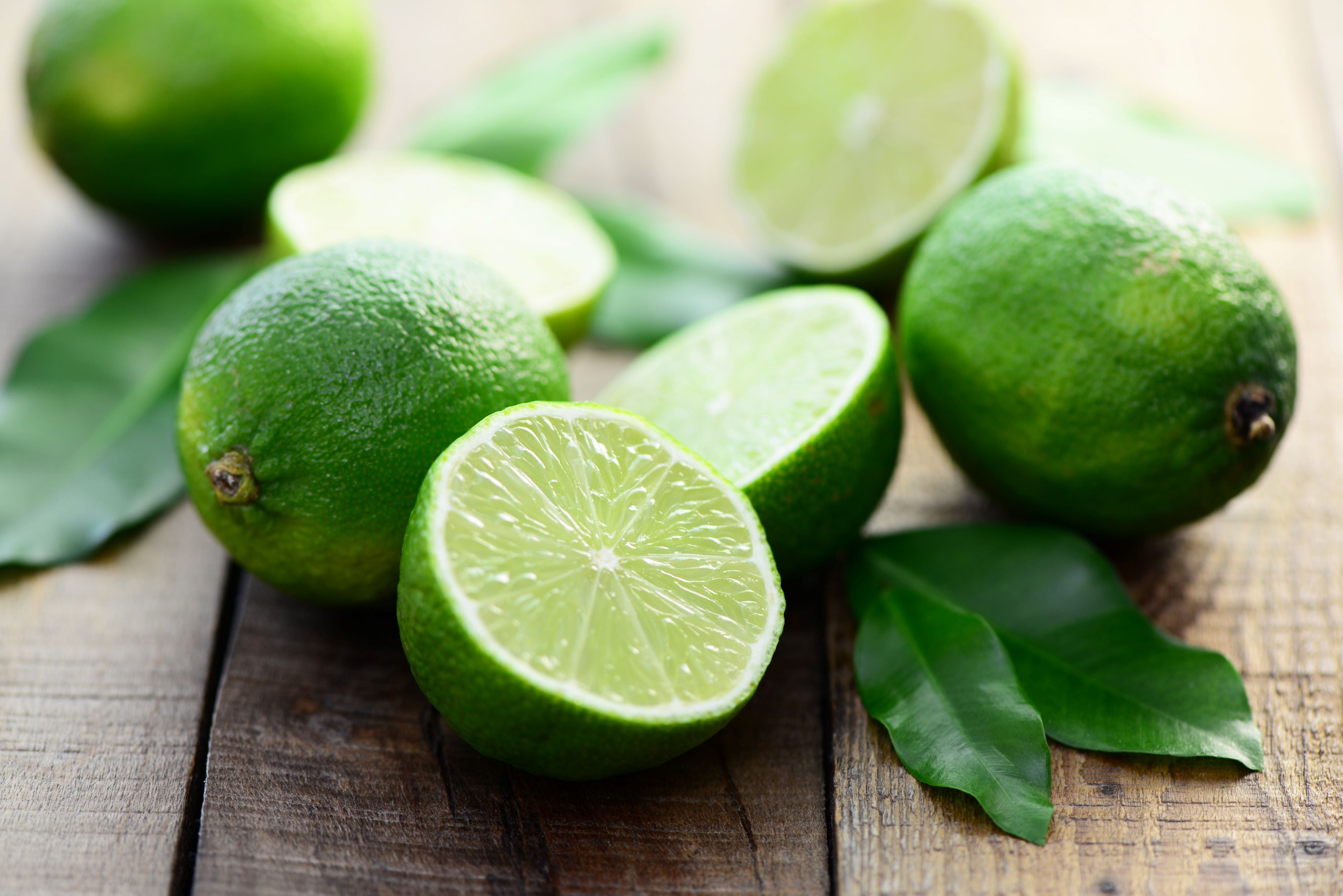Limetten zum Teil aufgeschnitten auf Holztisch zur Gewinnung von Limettenöl bio (kaltgepresst) - ätherischem Öl