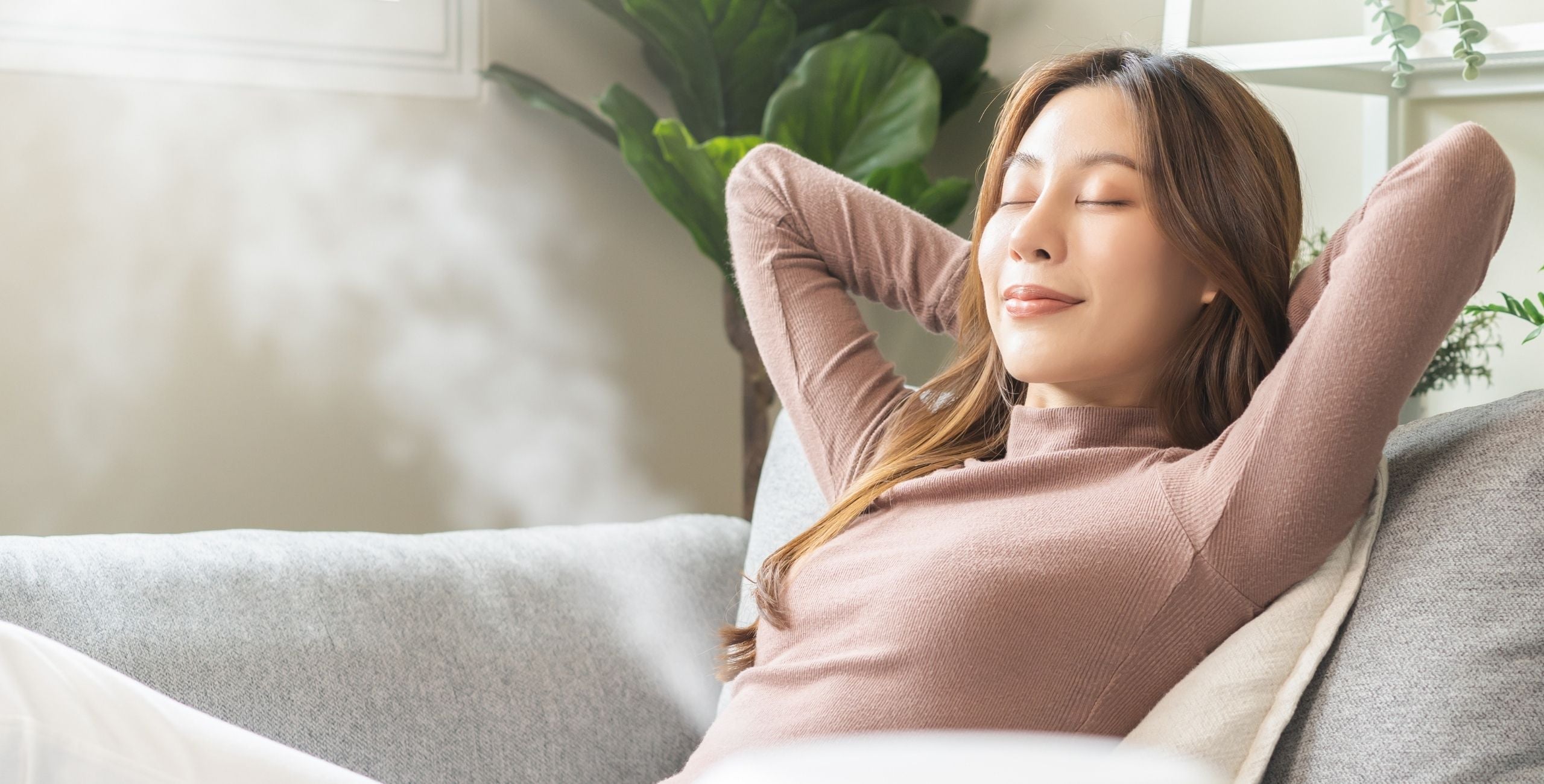 Entspannte Frau auf einem Sofa genießt den Duft ätherischer Öle aus einem Diffuser – Moment der Ruhe und Balance in natürlicher Atmosphäre.