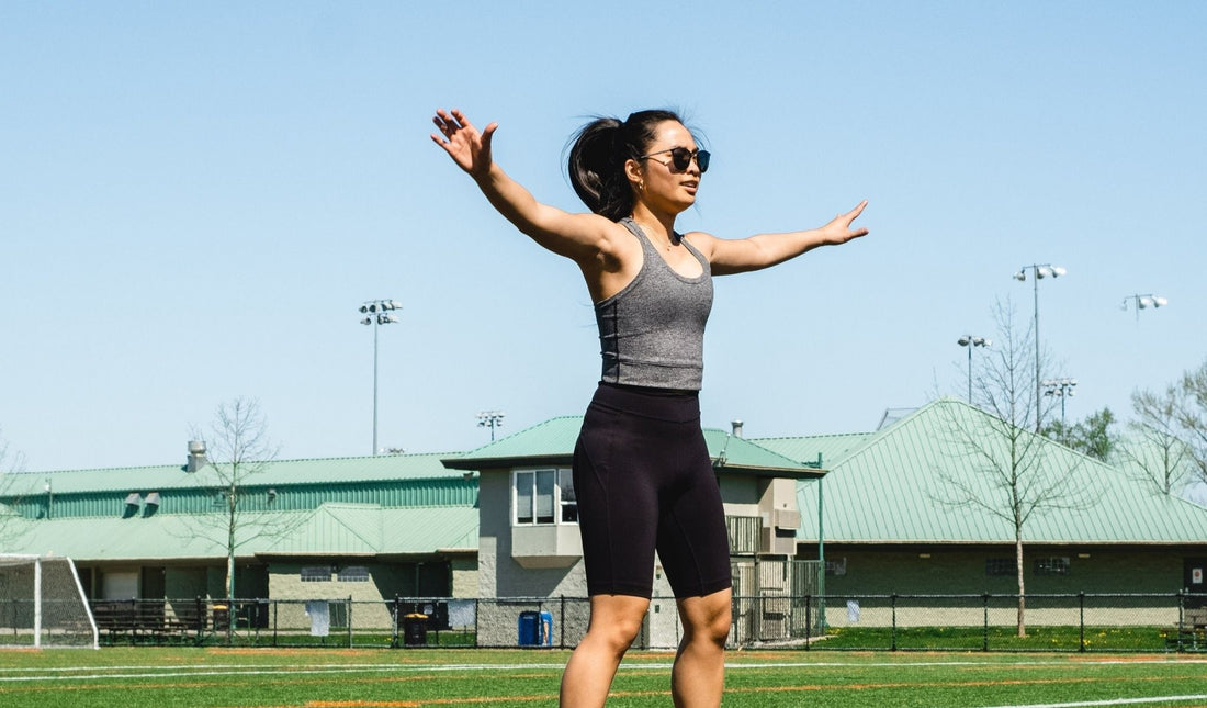 Frau macht Jumping Jacks auf einem Sportplatz bei Sonnenschein – symbolisiert Energie, Bewegung und Frische im Einklang mit der Natur.