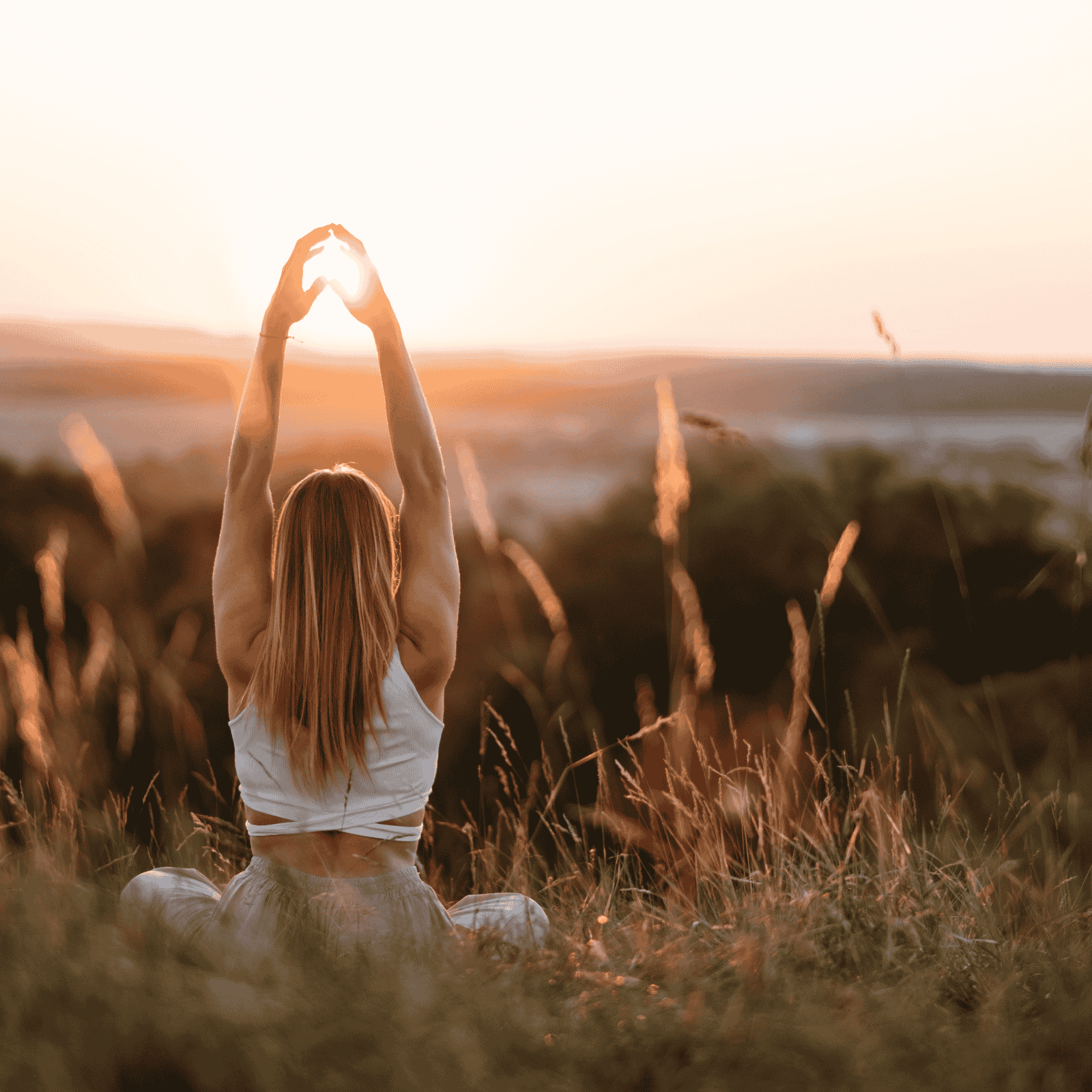 Frau sitzt meditierend im Gras bei Sonnenuntergang – Natur, Ruhe und Balance