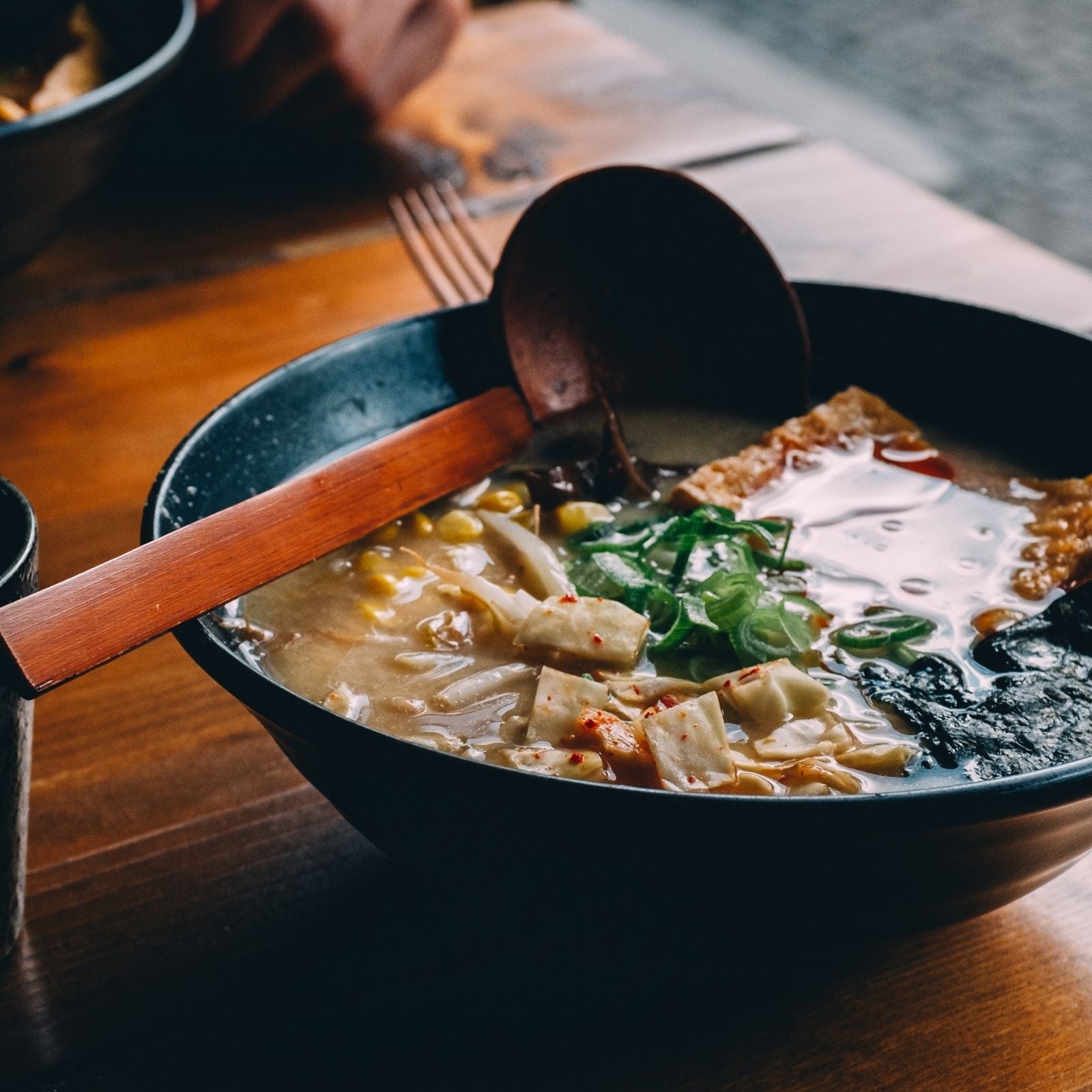 Schüssel mit dampfender, asiatischer Suppe auf einem Holztisch, garniert mit Tofu, Frühlingszwiebeln und Mais – ein Beispiel für aromatische Gerichte mit natürlichen Zutaten und ätherischen Gewürzölen.