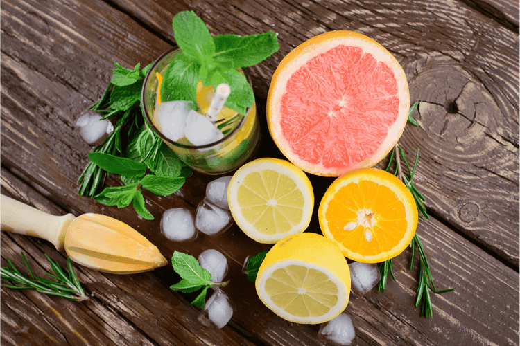 Minzblätter, Eiswürfel in einem Glas, daneben aufgeschnittene Grapefruit, Zitrone und Orange. Verziert mit frischem Rosmarin.
