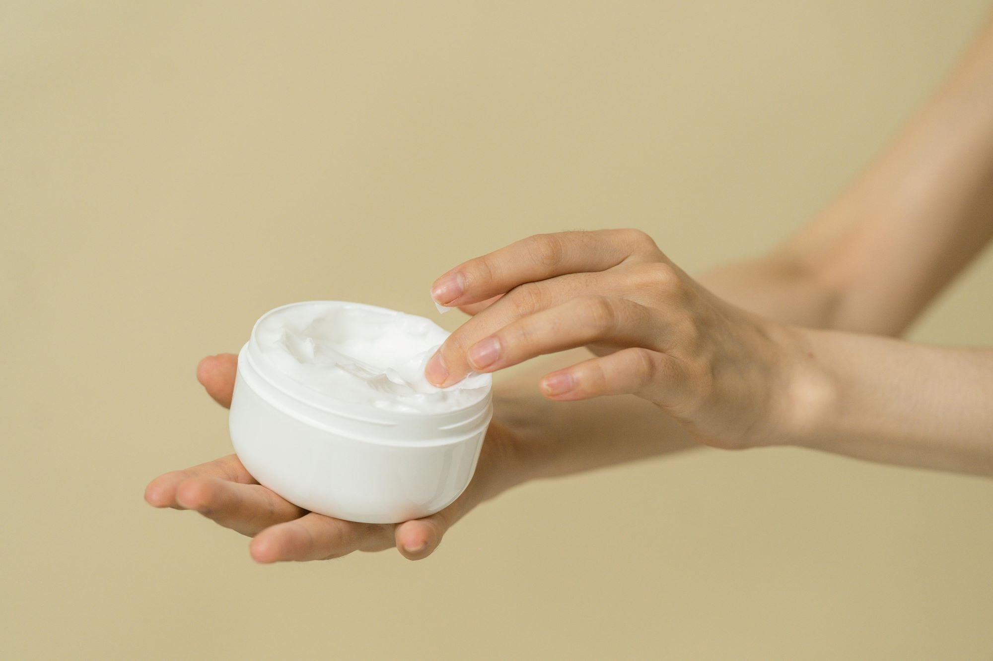 Hand entnimmt sanft eine kleine Menge Creme aus einem weißen Tiegel – Symbol für natürliche Hautpflege und achtsame Anwendung.