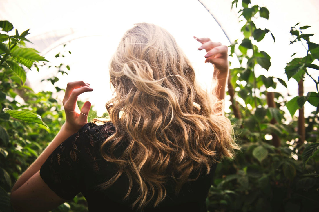 Natürlich schöne Haare – Frau mit langen, gewellten Haaren inmitten grüner Pflanzen.