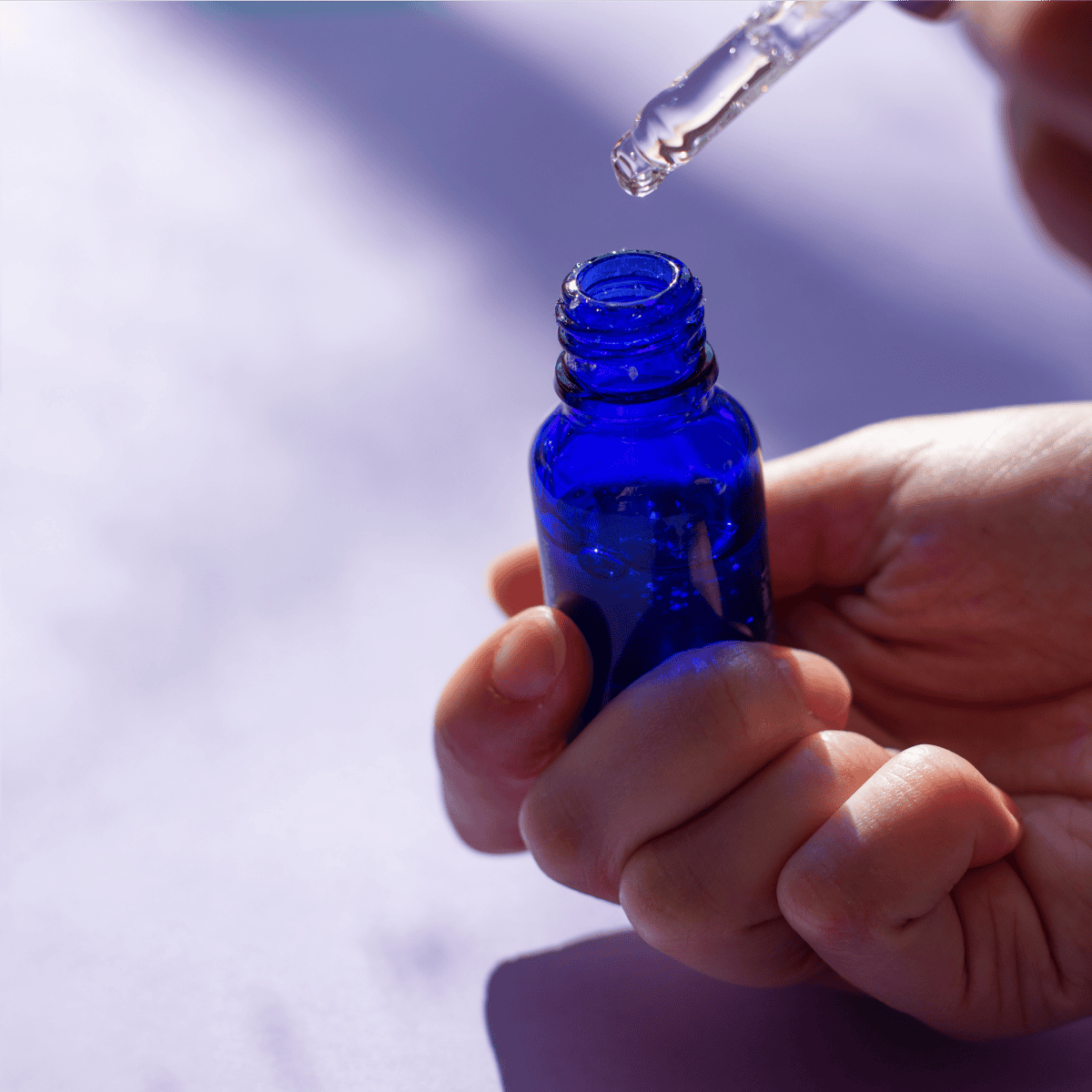 Hand mit Pipette und blauer Glasflasche – Symbol für vorsichtige Dosierung und sicheren Umgang mit ätherischen Ölen