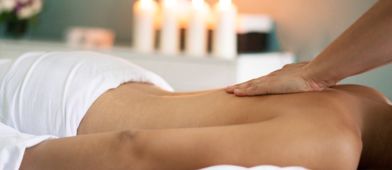 Eine Frau bekommt eine wohltuende Rückenmassage mit ätherischen Ölen im Schein von vier Kerzen.